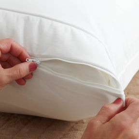 Image of a white pillow protector on a pillow with two hands zipping the protector closed 