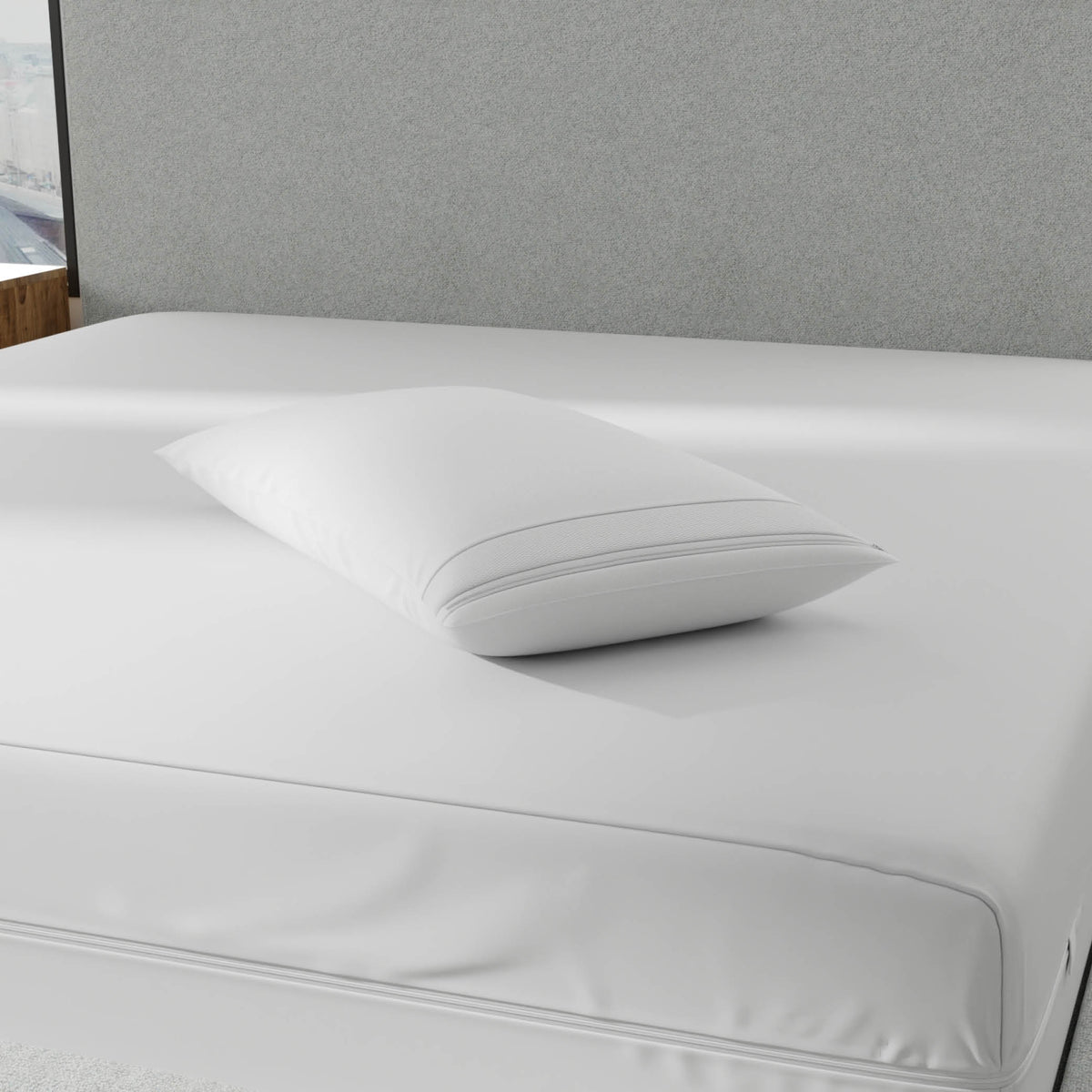 Image of a pillow with a white pillow protector on it laying on top of a bed with a gray headboard and white mattress protector on it