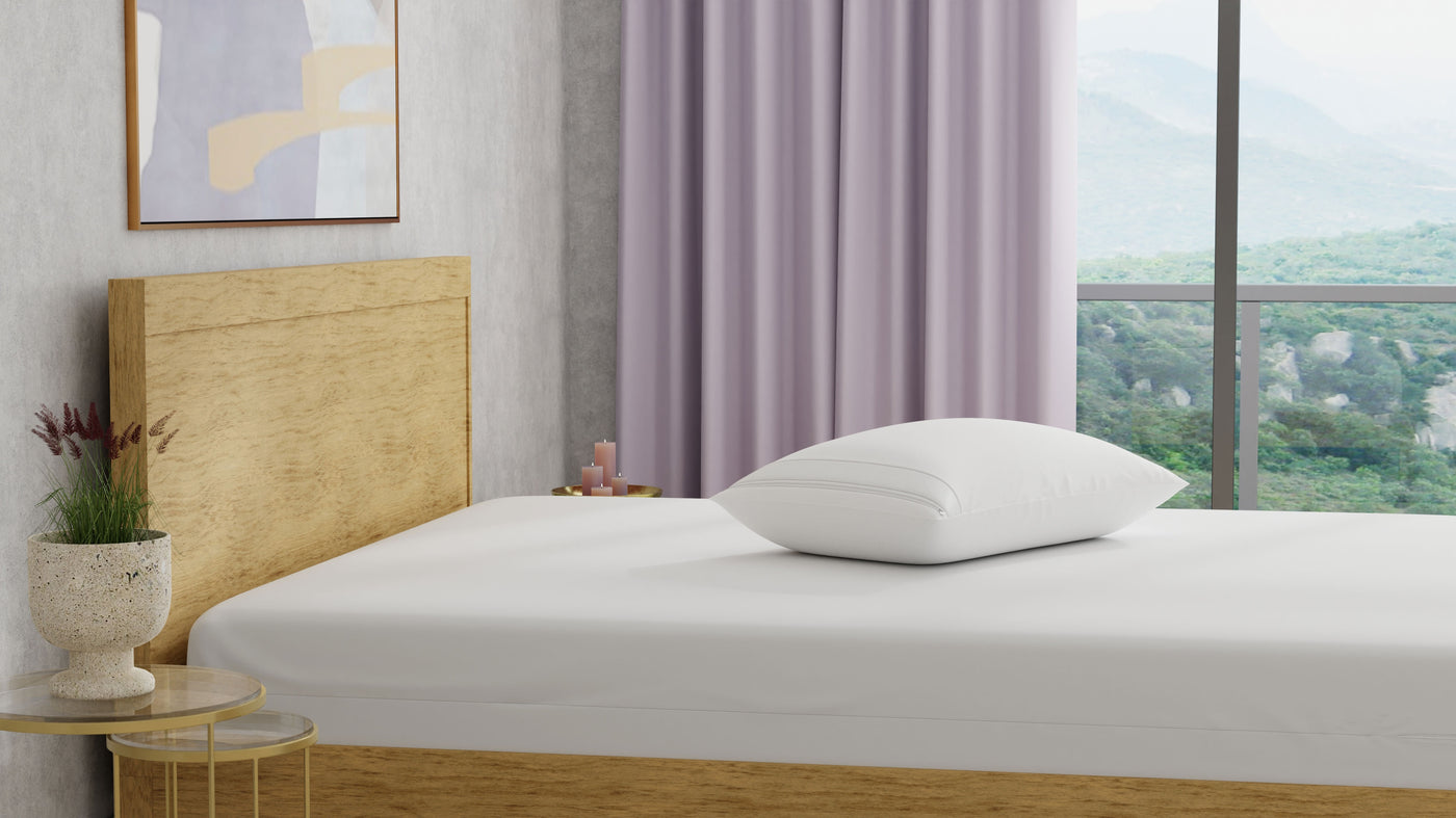 Image of a bed with just a mattress protector and pillow with pillow protector on it in a light-colored room with lilac-colored decorations