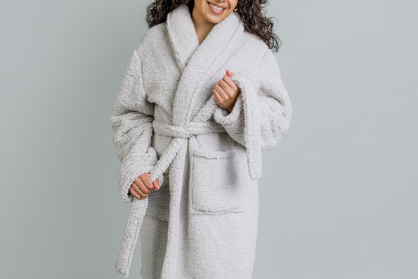 Image of a woman smiling and wearing the Sunday Morning Robe with her hands pulling at the belt