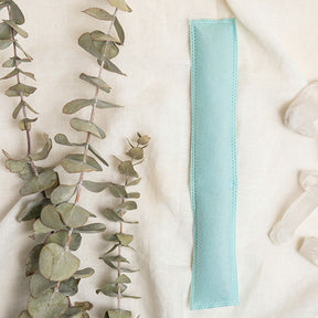 Image of a green Aromatherapy sachet with eucalyptus sprigs to the left of it and crystals to the right on an off-white fabric background