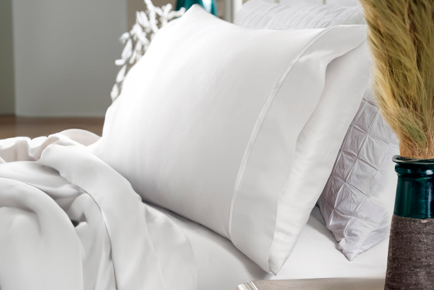 Image of a white pillowcase with pillow on a white bed with various decor in the room