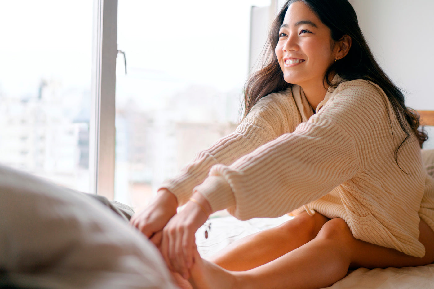 Image of a girl smiling, sitting on her bed, looking out the window