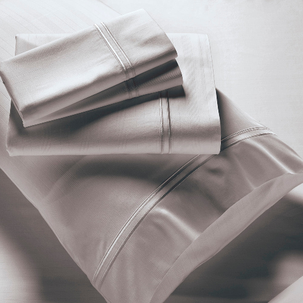 Image showcasing entire Dove Gray Bamboo Rayon Sheet Set. The image includes: a fitted sheet on the bed, a pillowcase on a pillow, a neatly folded flat sheet, and two neatly folded pillowcases.