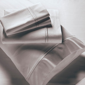 Image showcasing entire Dove Gray Bamboo Rayon Sheet Set. The image includes: a fitted sheet on the bed, a pillowcase on a pillow, a neatly folded flat sheet, and two neatly folded pillowcases.