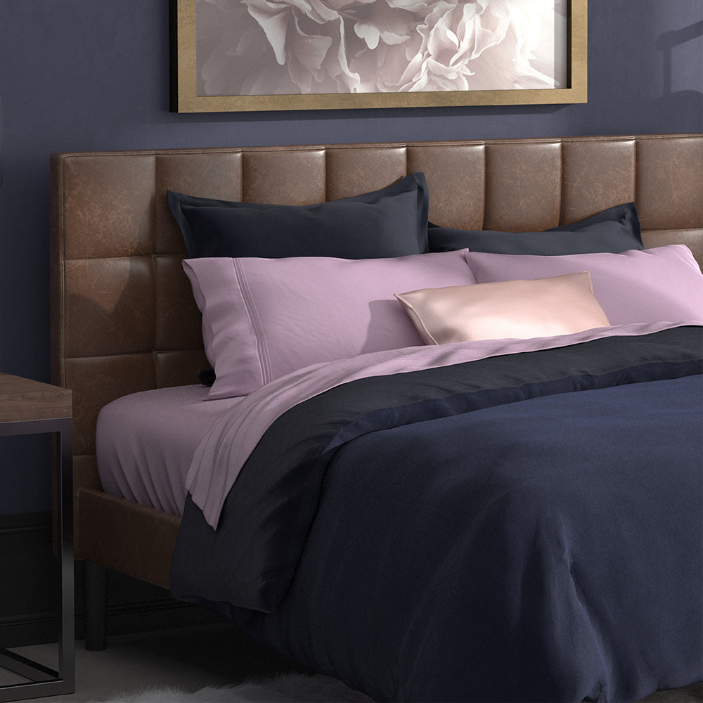 Image of a neatly made bed with Lilac Bamboo Rayon Sheets and other navy blue and pink layers added 