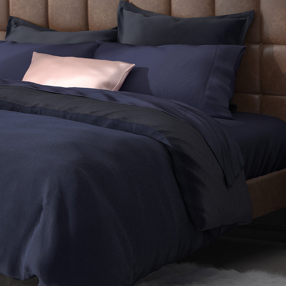 Image of a neatly made bed with Midnight Bamboo Rayon Sheets on it with other navy blue and soft pink layers