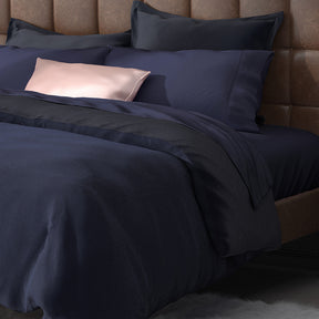 Image of a neatly made bed with Midnight Bamboo Rayon Sheets on it with other navy blue and soft pink layers