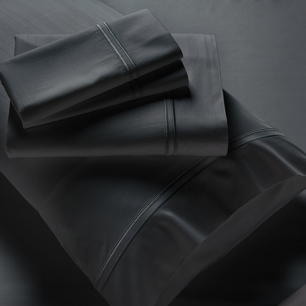Image showcasing entire Shadow Bamboo Rayon Sheet Set. The image includes: a fitted sheet on the bed, a pillowcase on a pillow, a neatly folded flat sheet, and two neatly folded pillowcases.