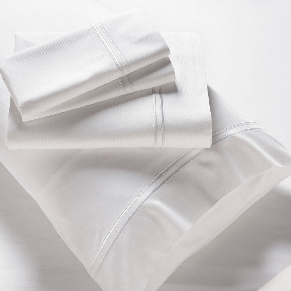 Image showcasing entire White Bamboo Rayon Sheet Set. The image includes: a fitted sheet on the bed, a pillowcase on a pillow, a neatly folded flat sheet, and two neatly folded pillowcases.