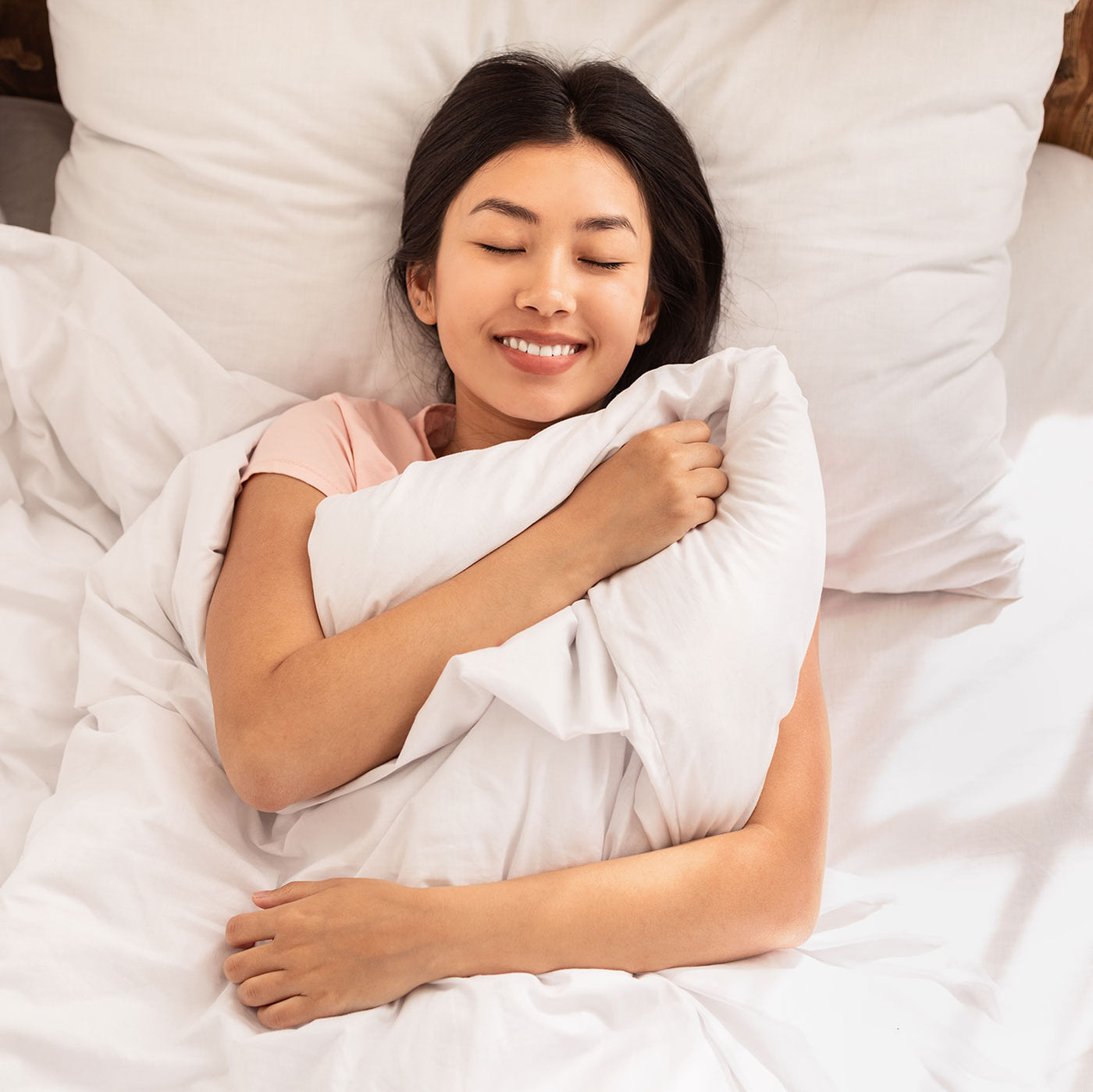 Image of a woman asleep in bed holding her white duvet against her