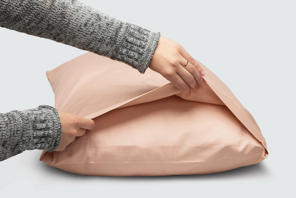 Image of two hands holding open the side of a Blush Pink Weightless Cotton Pillowcase showcasing the enveloping design
