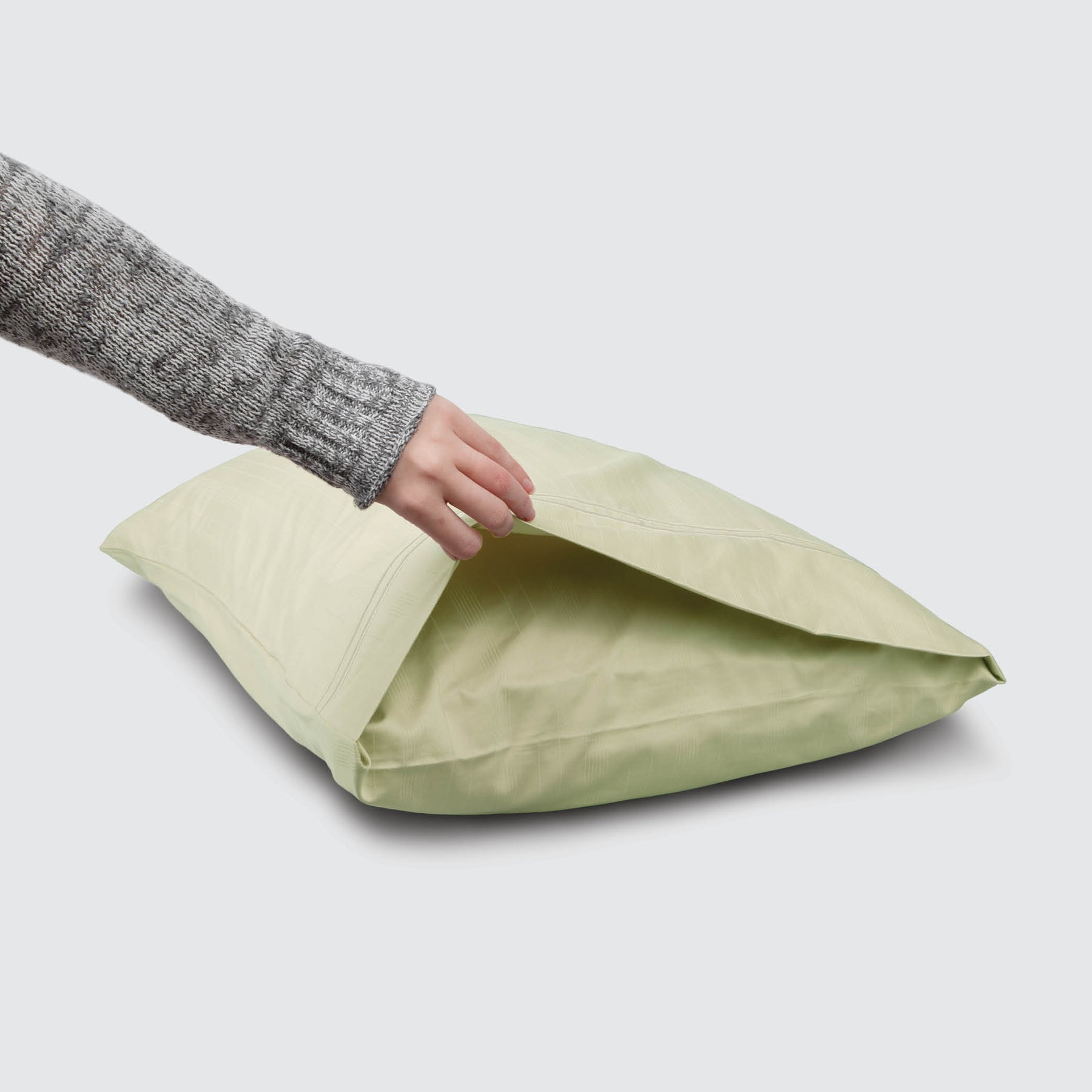 Image of a Sage Bamboo Rayon Pillowcase on a pillow with a hand lifting up the edge to showcase the enveloping design