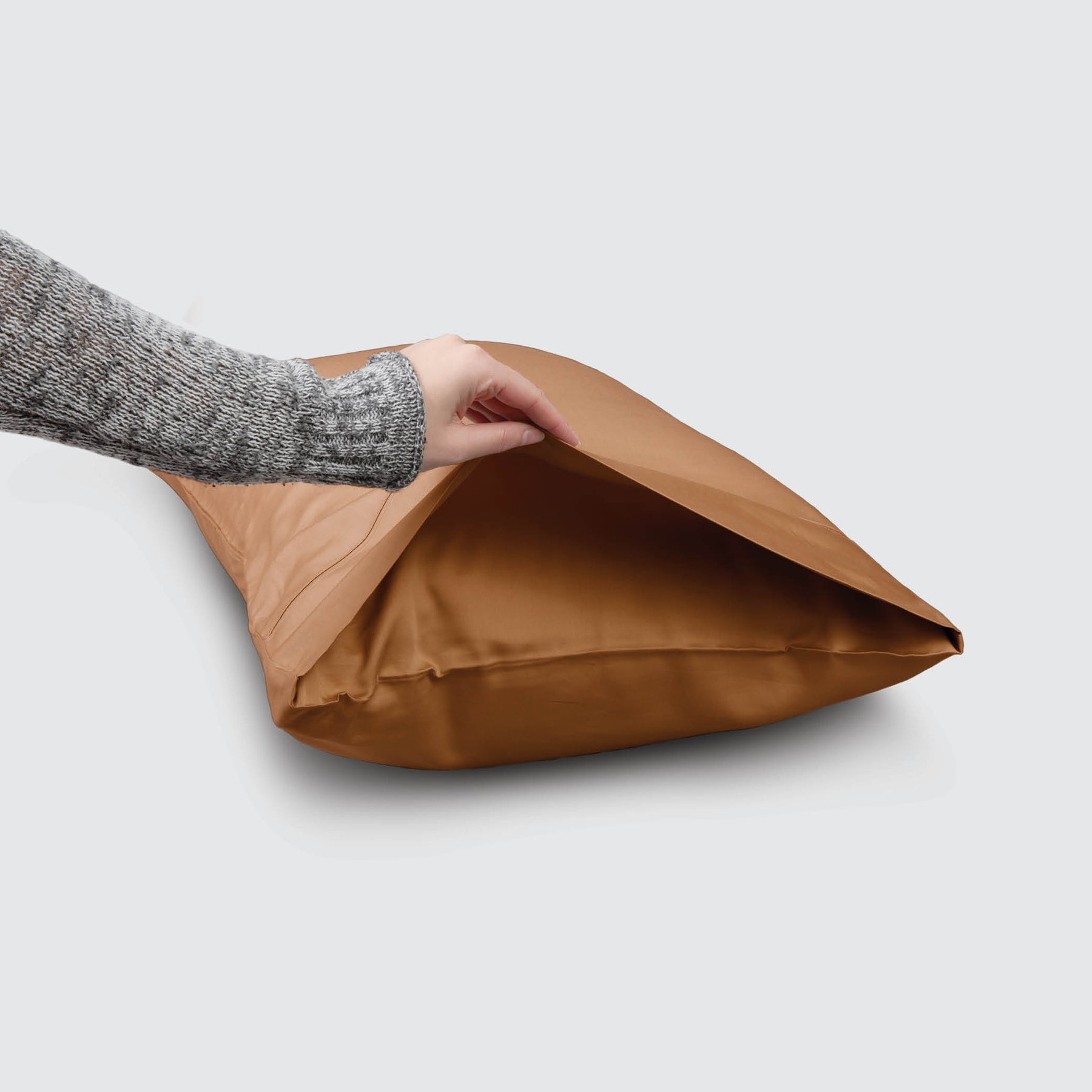 Image of a Clay Recovery Viscose Pillowcase on a pillow with a hand lifting up the edge to showcase the enveloping design