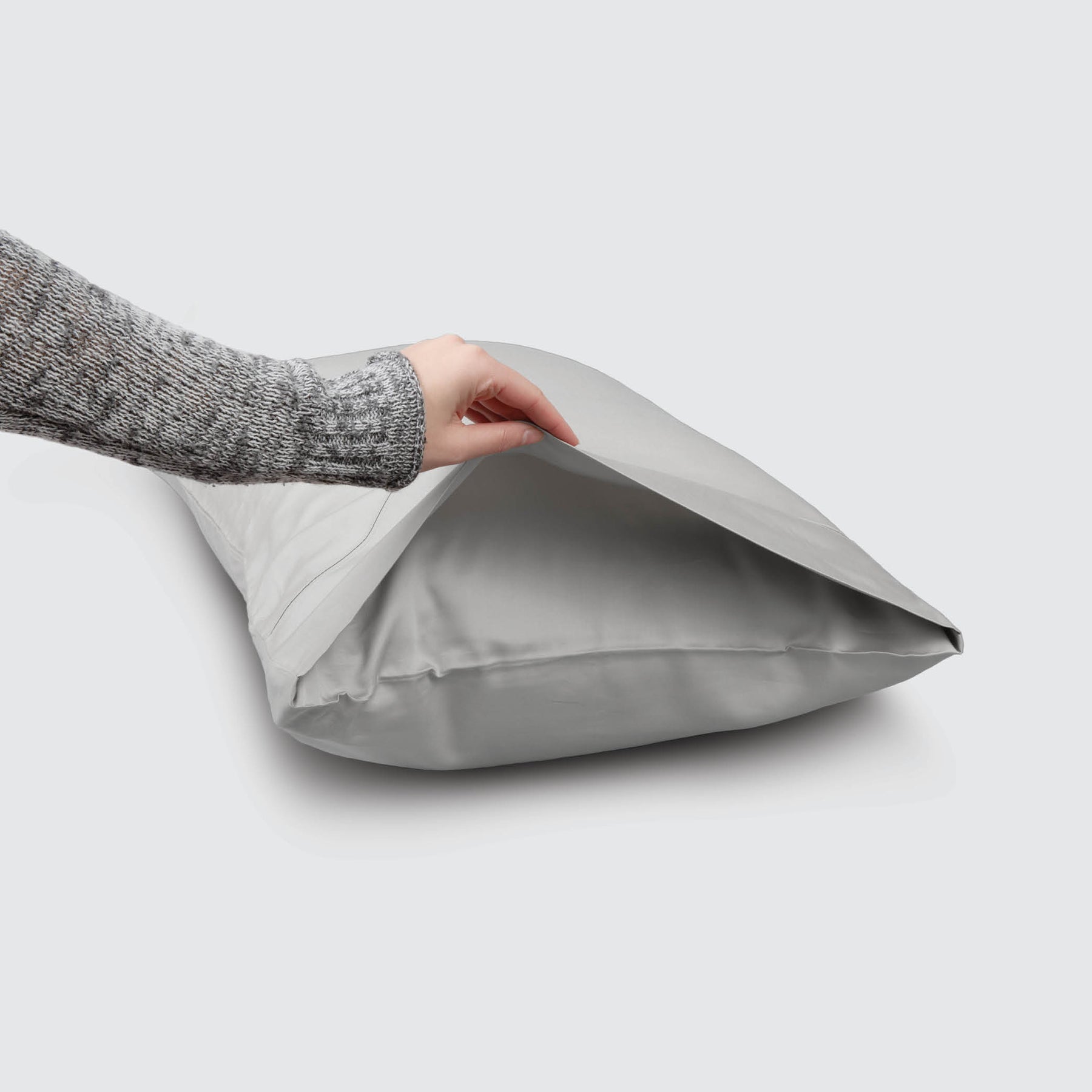 Image of a Dove Gray Recovery Viscose Pillowcase on a pillow with a hand lifting up the edge to showcase the enveloping design