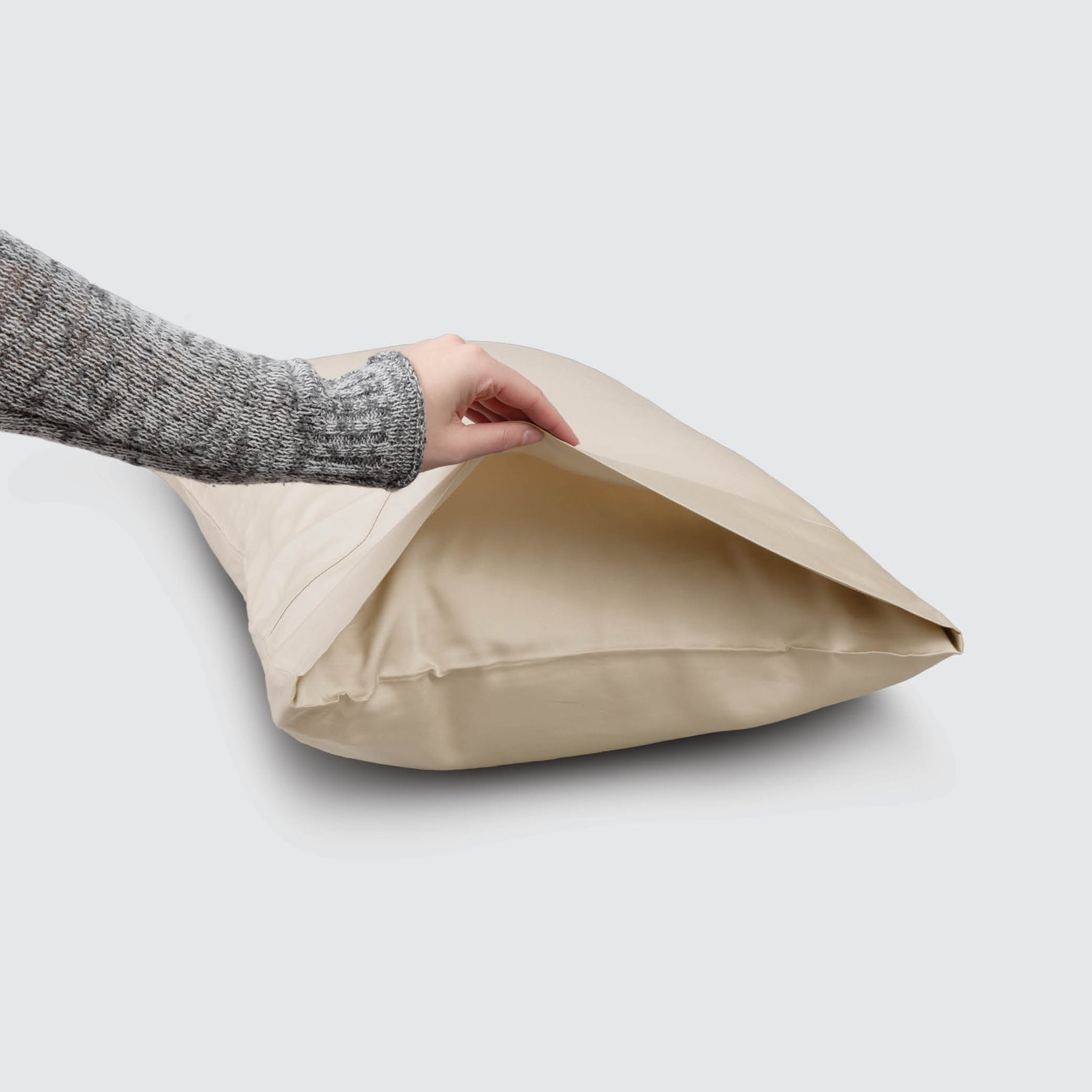 Image of an Ivory Recovery Viscose Pillowcase on a pillow with a hand lifting up the edge to showcase the enveloping design