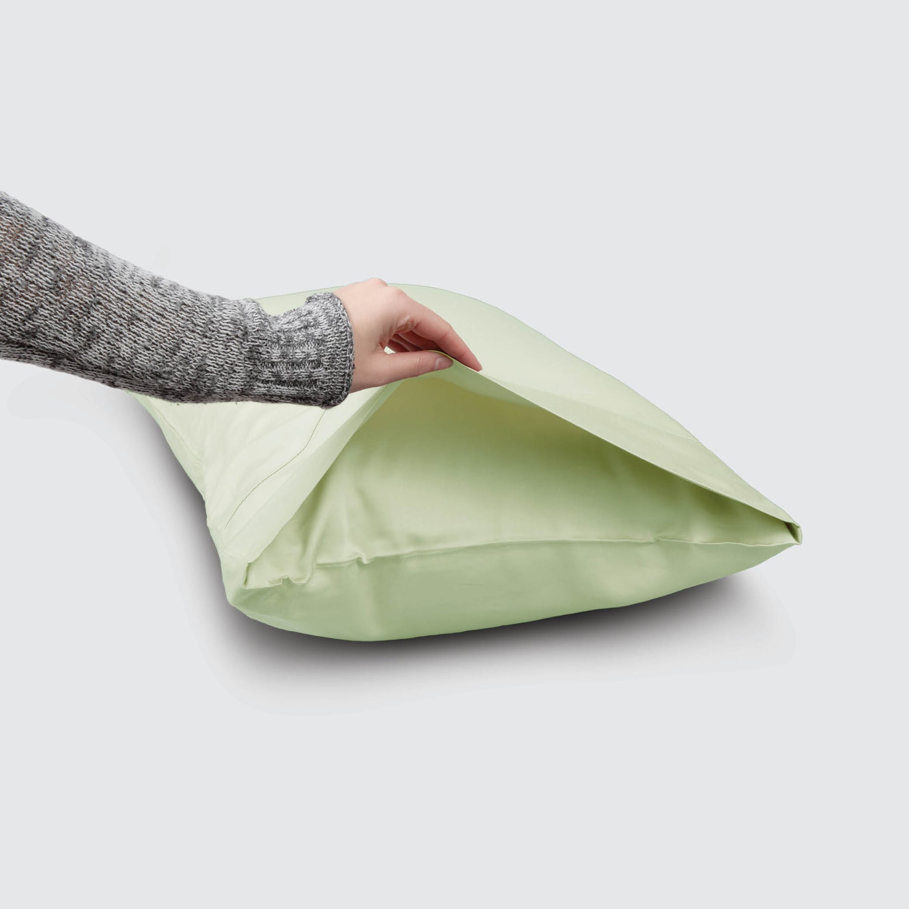 Image of a Sage Recovery Viscose Pillowcase on a pillow with a hand lifting up the edge to showcase the enveloping design
