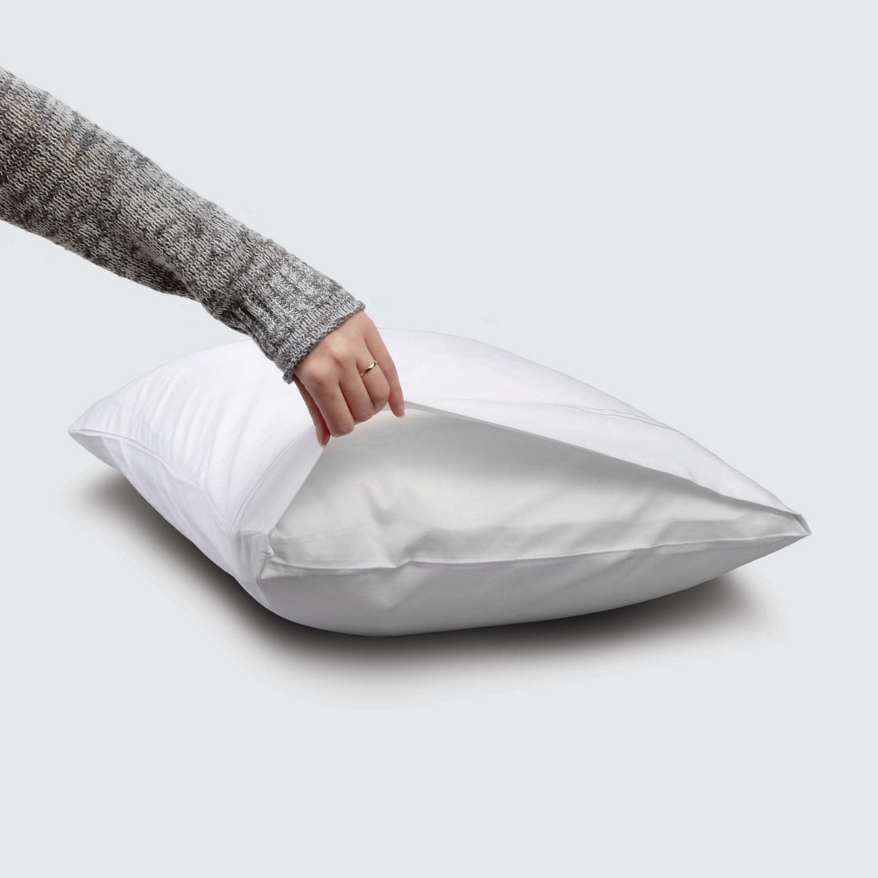 Image of a White Refreshing TENCEL™ Lyocell Pillowcase on a pillow with a hand lifting up the edge to showcase the enveloping design