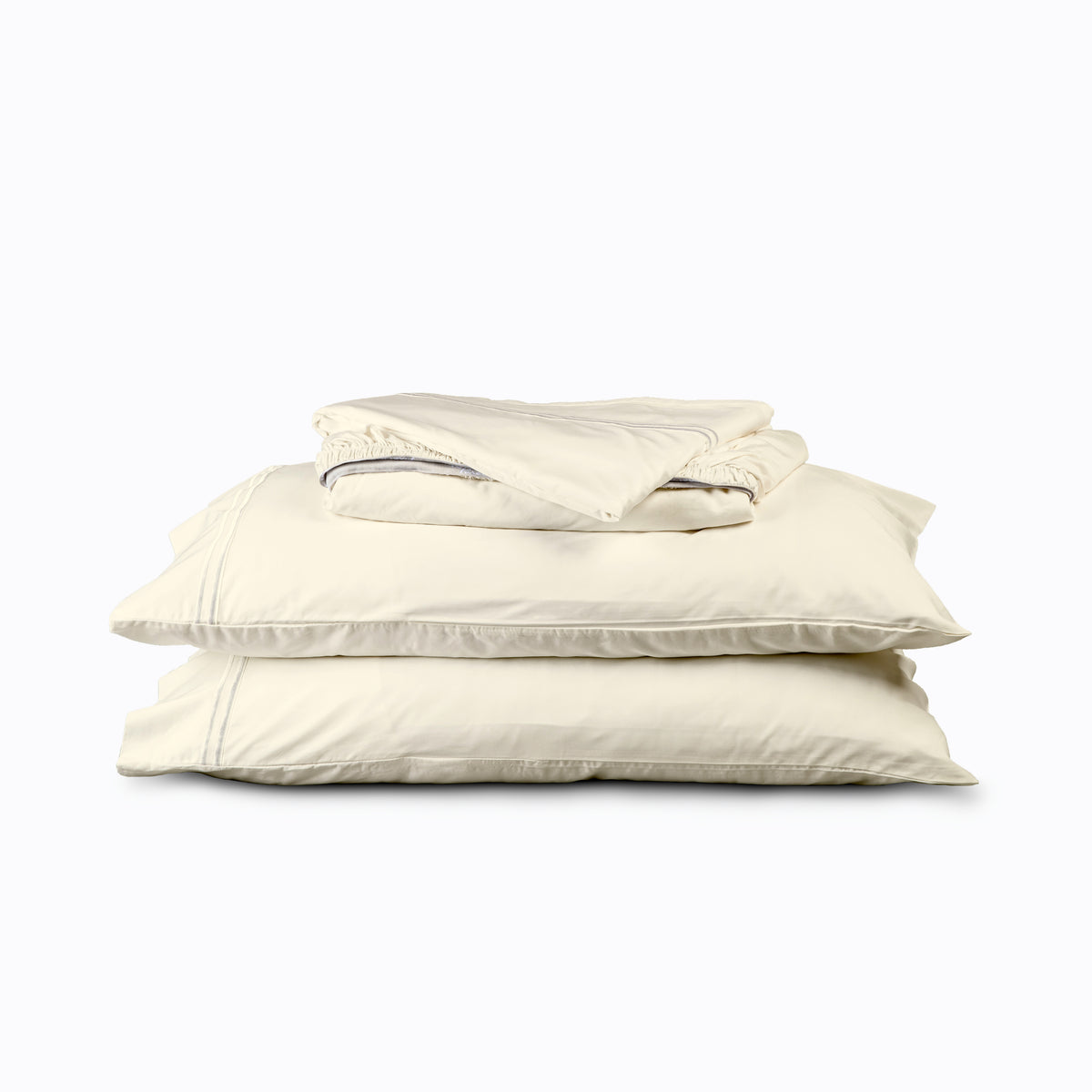 Image of an Ivory Soft Touch TENCEL™ Modal sheet stack that includes (from top to bottom): a folded flat sheet, a folded fitted sheet, and two pillowcases on pillows