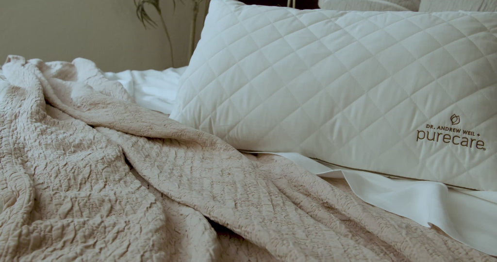 Video of hand softly feeling and squeezing the All Seasons Wool Pillow on a neutral-colored bed