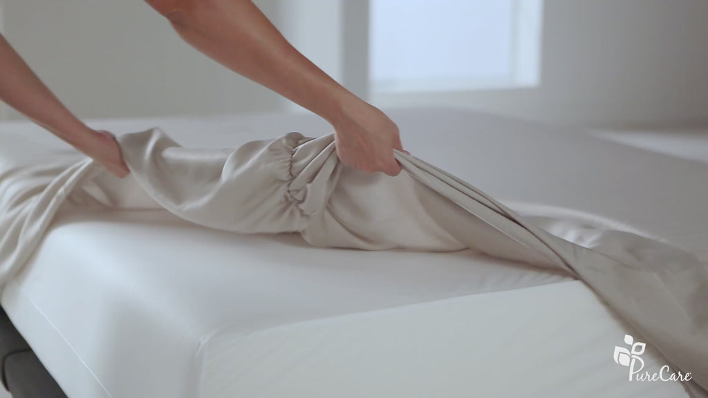 Video of a person pulling their fitted sheet over the bottom of the mattress highlighting the Precision-Fit® Elastic band and corners. The person then lays a flat sheet on the bed. The video moves to a white table where the person showcases the enveloping design with the pillow not falling out of the pillowcase. 