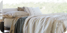 Image of a made bed with a large window behind it. The bed showcases Ochre Garment Washed Percale Sheets, an Agave Ridgeback Coverlet, and a Sonoran Duvet Cover.
