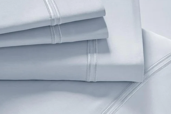 Image showcasing a Light Blue Sheet Set. The image includes: a fitted sheet on the bed, a pillowcase on a pillow, a neatly folded flat sheet, and two neatly folded pillowcases.