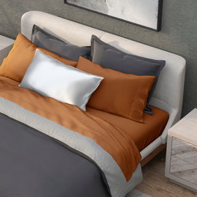 Image of a neatly made bed with a dark gray duvet and the Clay Recovery Viscose Sheet Set and Pillowcases