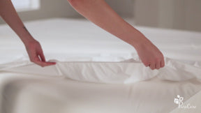 Video of a person putting a Mattress Protector on a mattress. The video then shows a cup of spilled water on the protector. The person pulls the protector up showing that there was no moisture underneath. The person then takes the protector off and places it in a laundry basket.