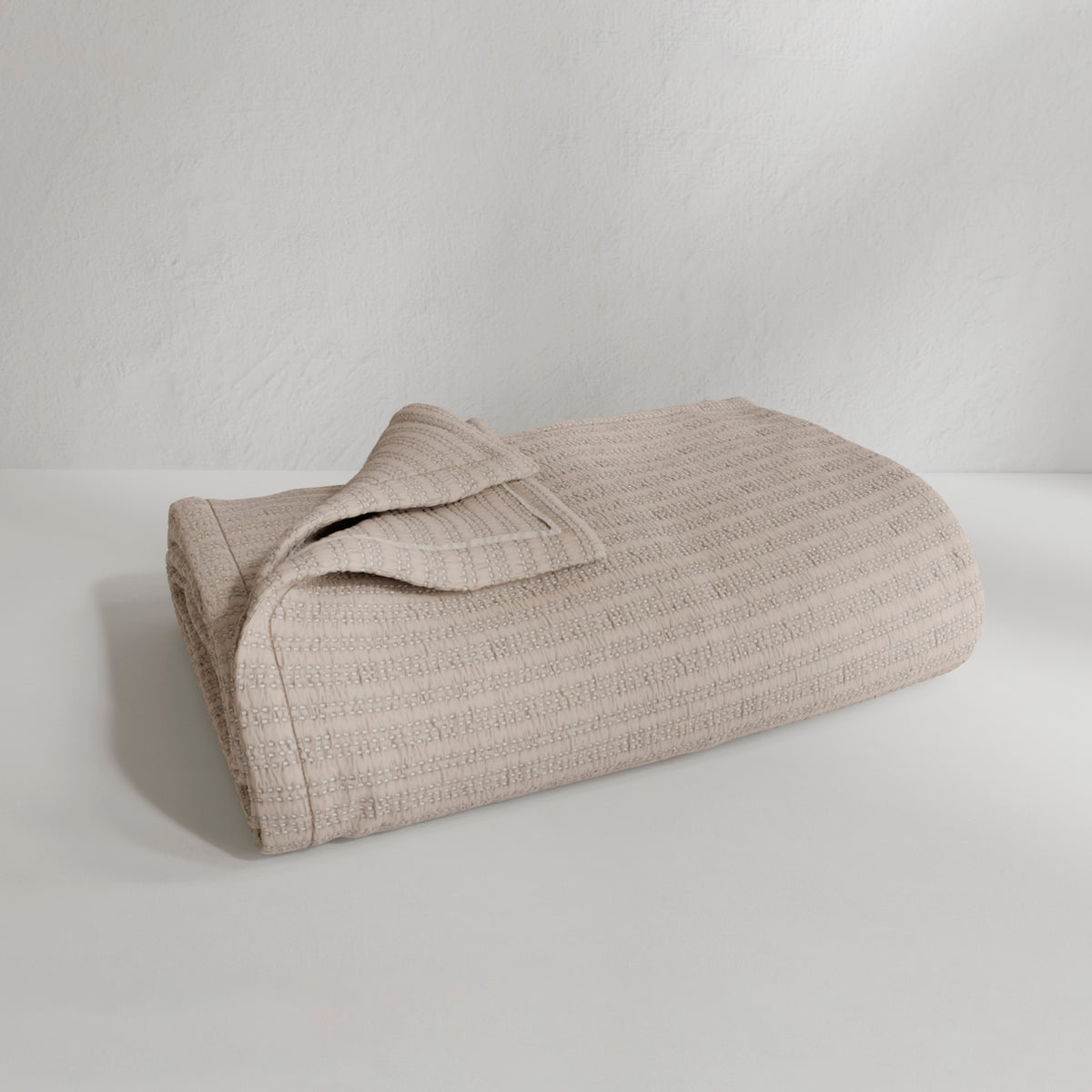 Image of a neatly folded Oatmeal Everyday Cotton Coverlet with the back left corner folded up on a white background
