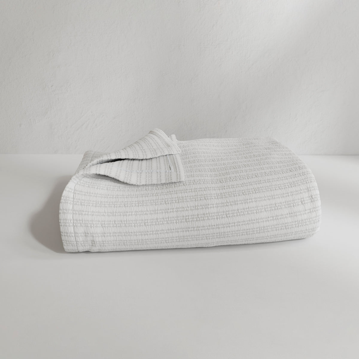 Image of a neatly folded Bright White Everyday Cotton Coverlet with the back left corner folded up on a white background