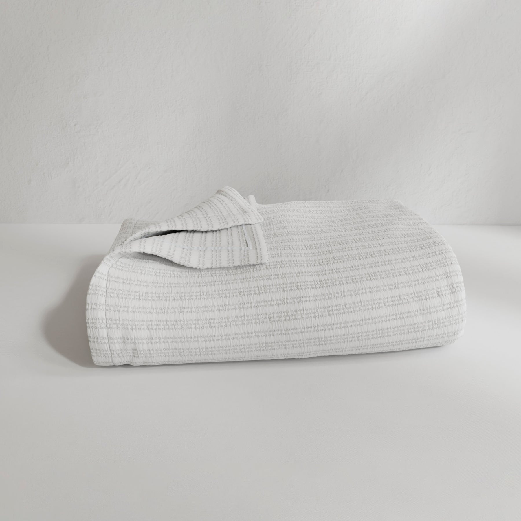 Image of a neatly folded Bright White Everyday Cotton Coverlet with the back left corner folded up on a white background
