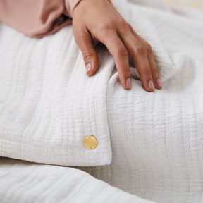 Image of a hand resting on the Bright White Everyday Cotton Coverlet