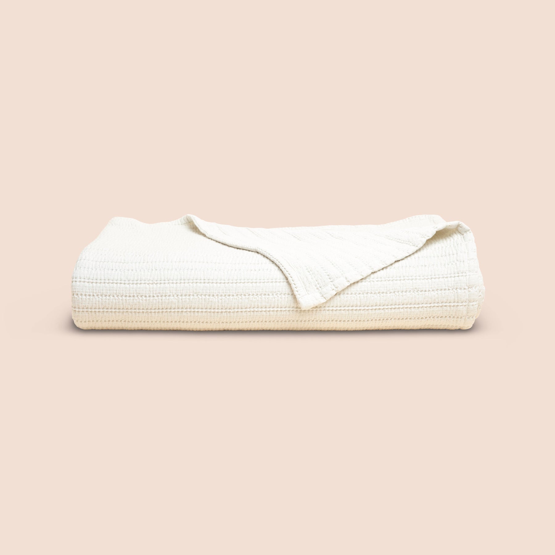 Image of Ecru Ridgeback Coverlet neatly folded with one corner folded forward on a light pink background