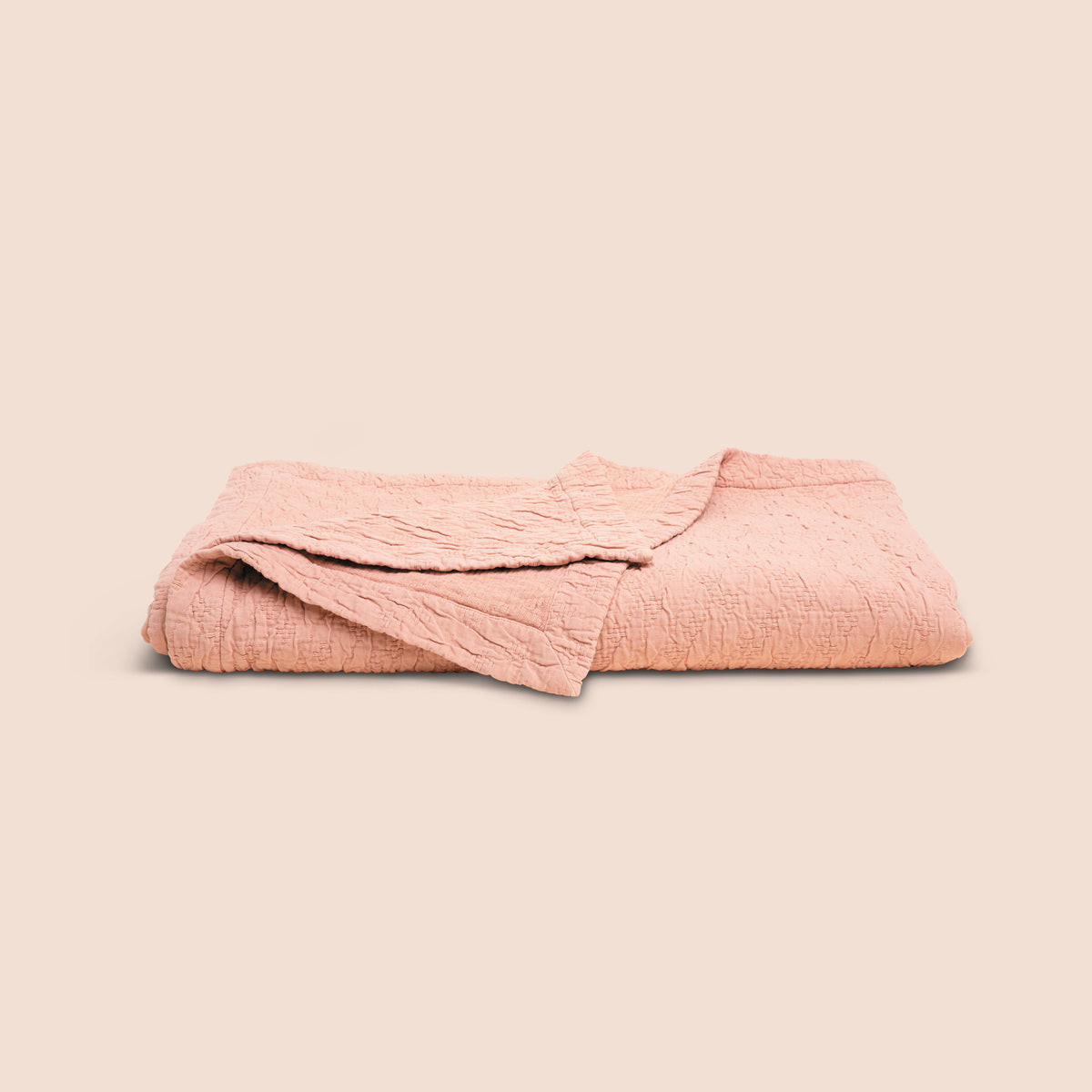 Image of the Pink Sandstone Wave Coverlet neatly folded with the back right corner folded forward on a light pink background