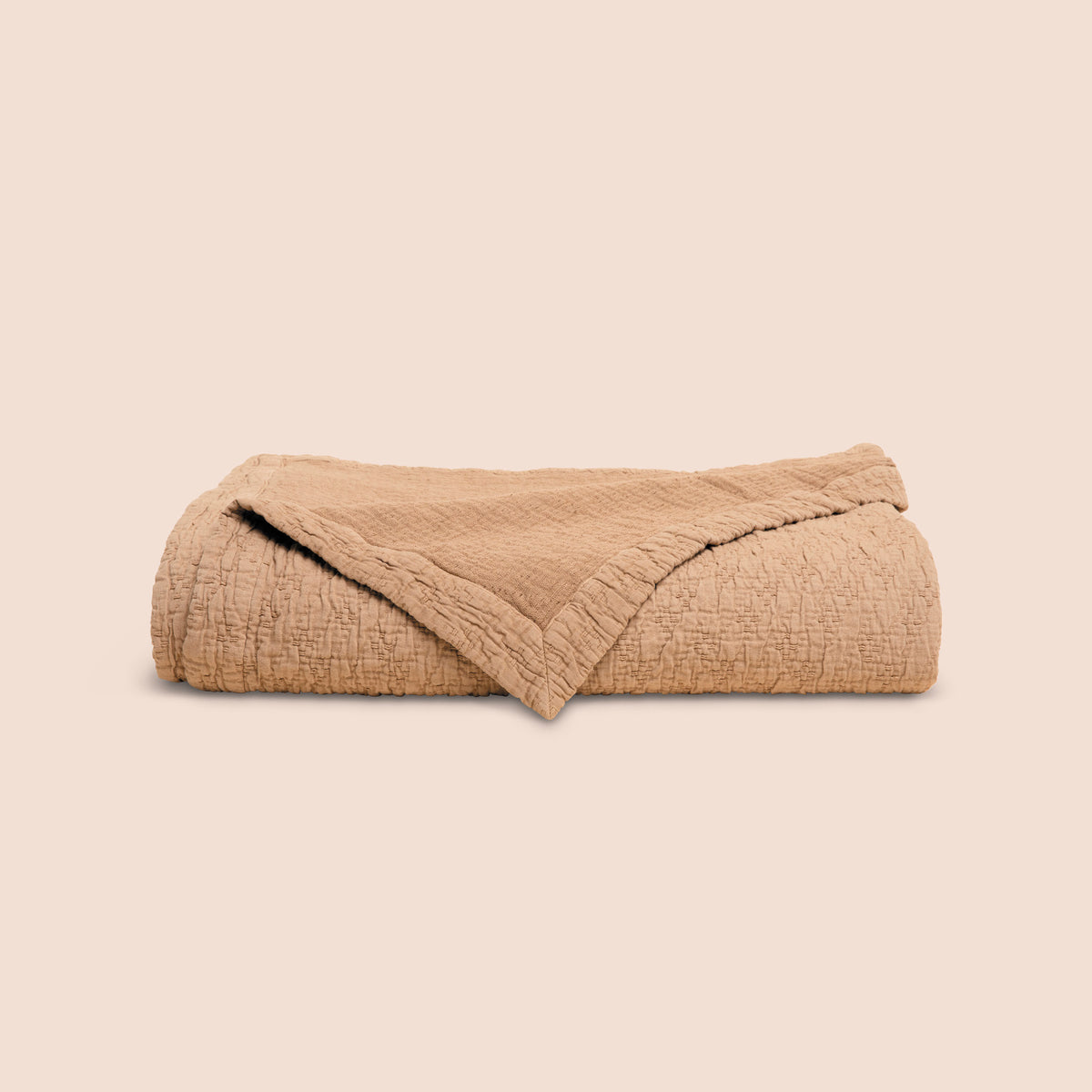 Image of the Ochre Wave Coverlet neatly folded with the back right corner folded forward on a light pink background