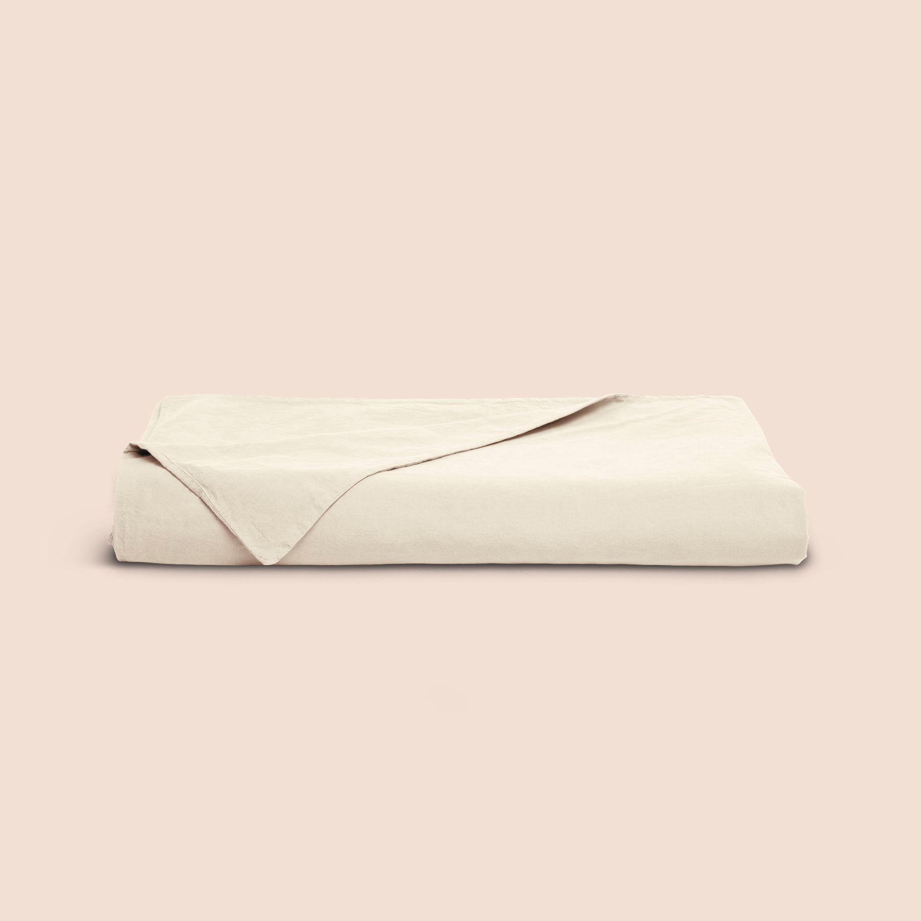 Image of an Ecru Garment Washed Percale Duvet Cover neatly folded with one corner draped towards the front on a light pink background