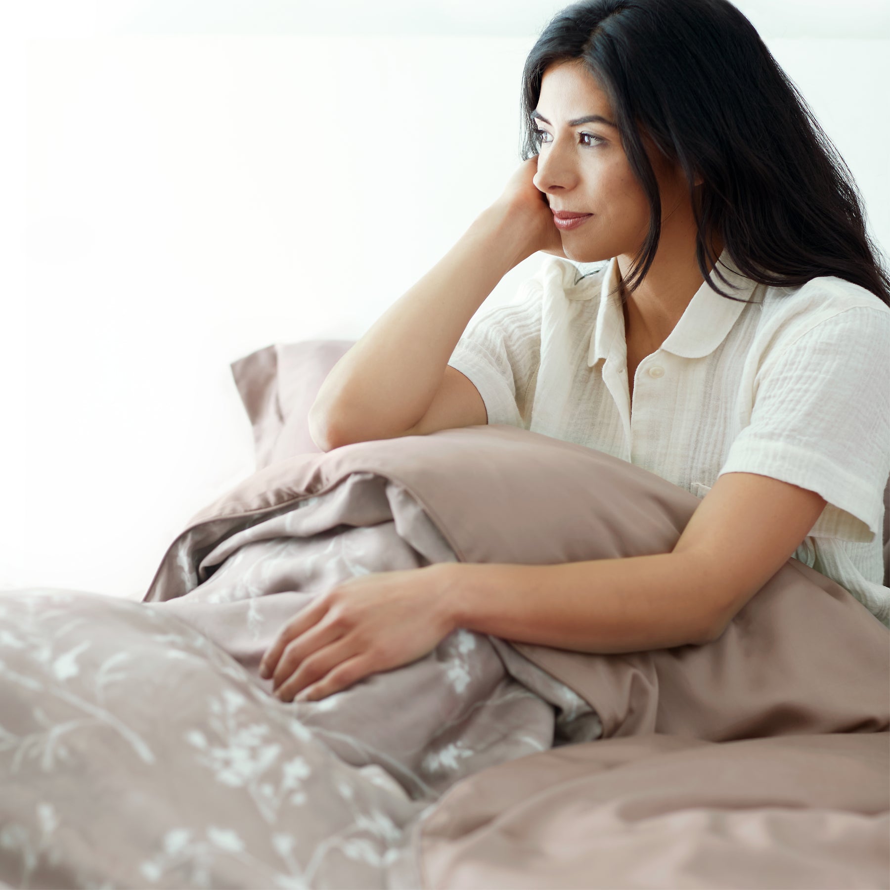 Image of a woman sitting up in bed covered with the Floral Oatmeal Duvet Cover + Cooling