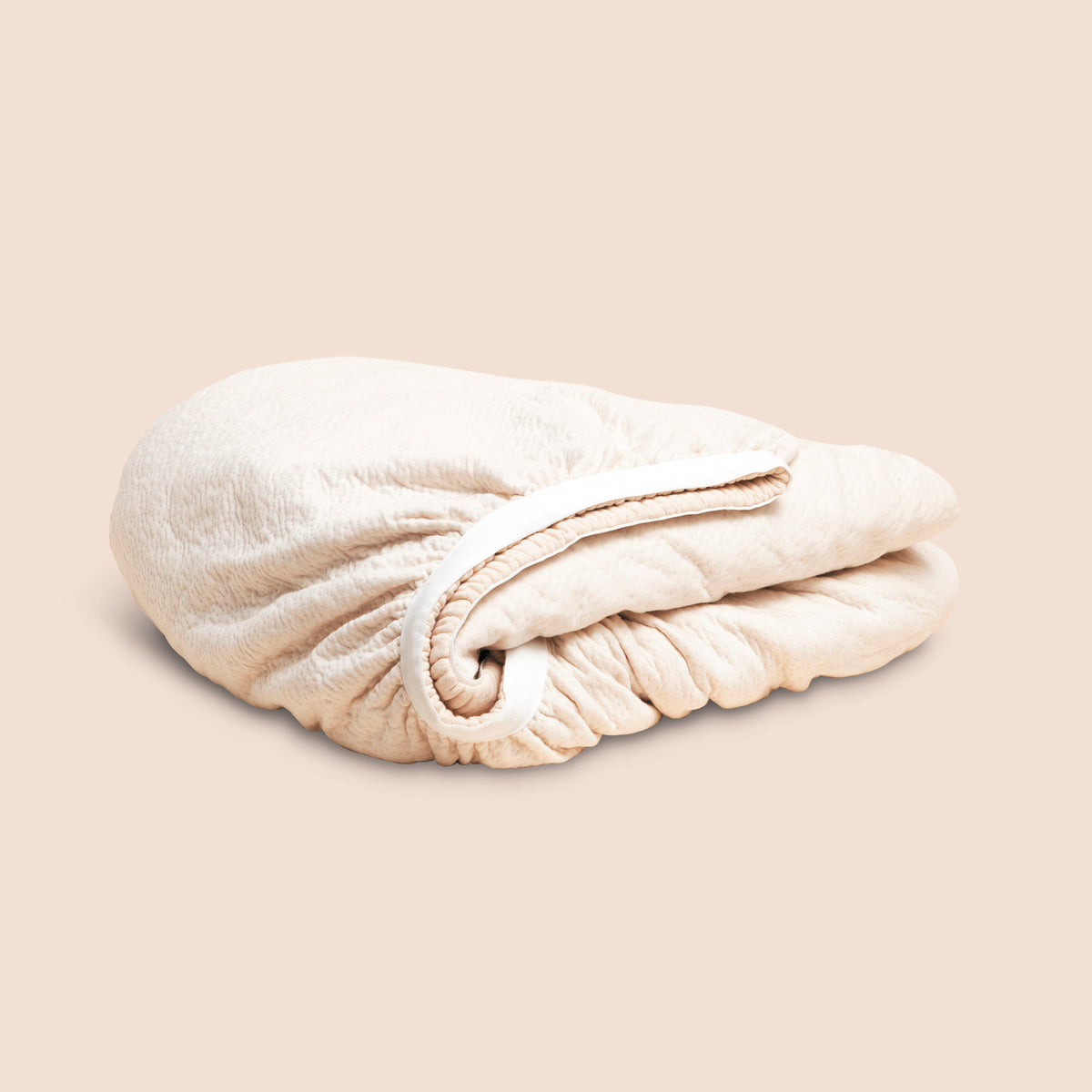 Image of a neatly folded off-white Signature Mattress Protector on a light pink background
