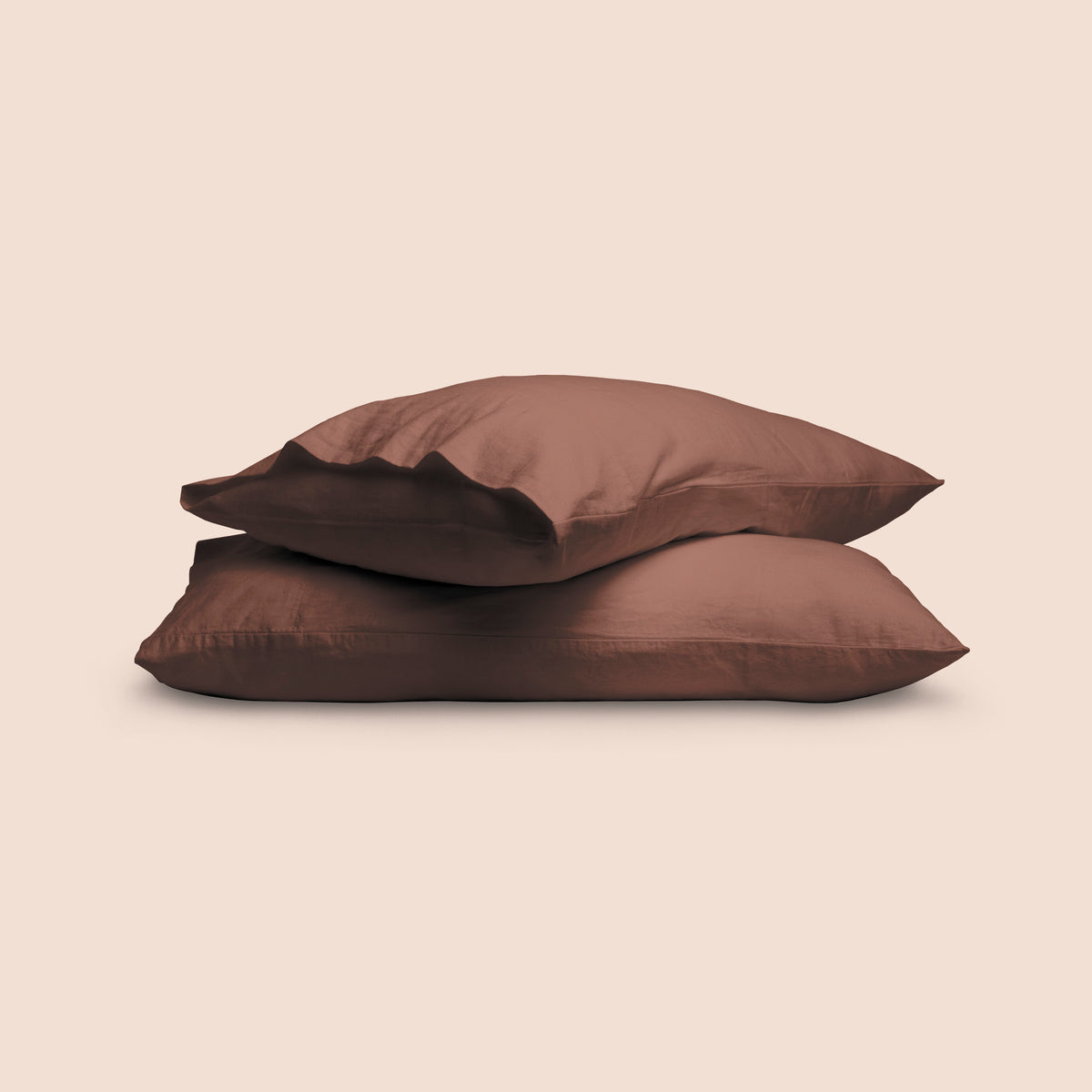 Image of two pillows with Cacao Blended Linen Pillowcases stacked on top of each other on a light pink background. The top pillow is showcasing an enveloping feature. 