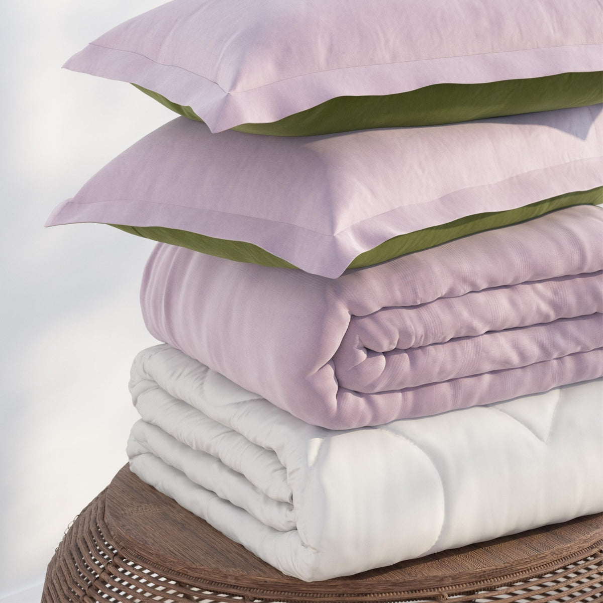 Image of a pile of bedding on top of a brown table. The bedding shown includes (from top to bottom): 2 Lilac/Jungle Pillow Shams with the Lilac side facing up, a neatly folded Lilac/Jungle Duvet Cover + Cooling with the lilac side showing, and a neatly folded Cooling Duvet Insert 
