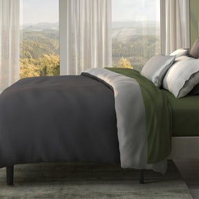 Image of a neatly made bed with moss-colored sheets and the Shadow/Dove Gray Duvet Cover + Cooling on top with the Shadow side facing up 