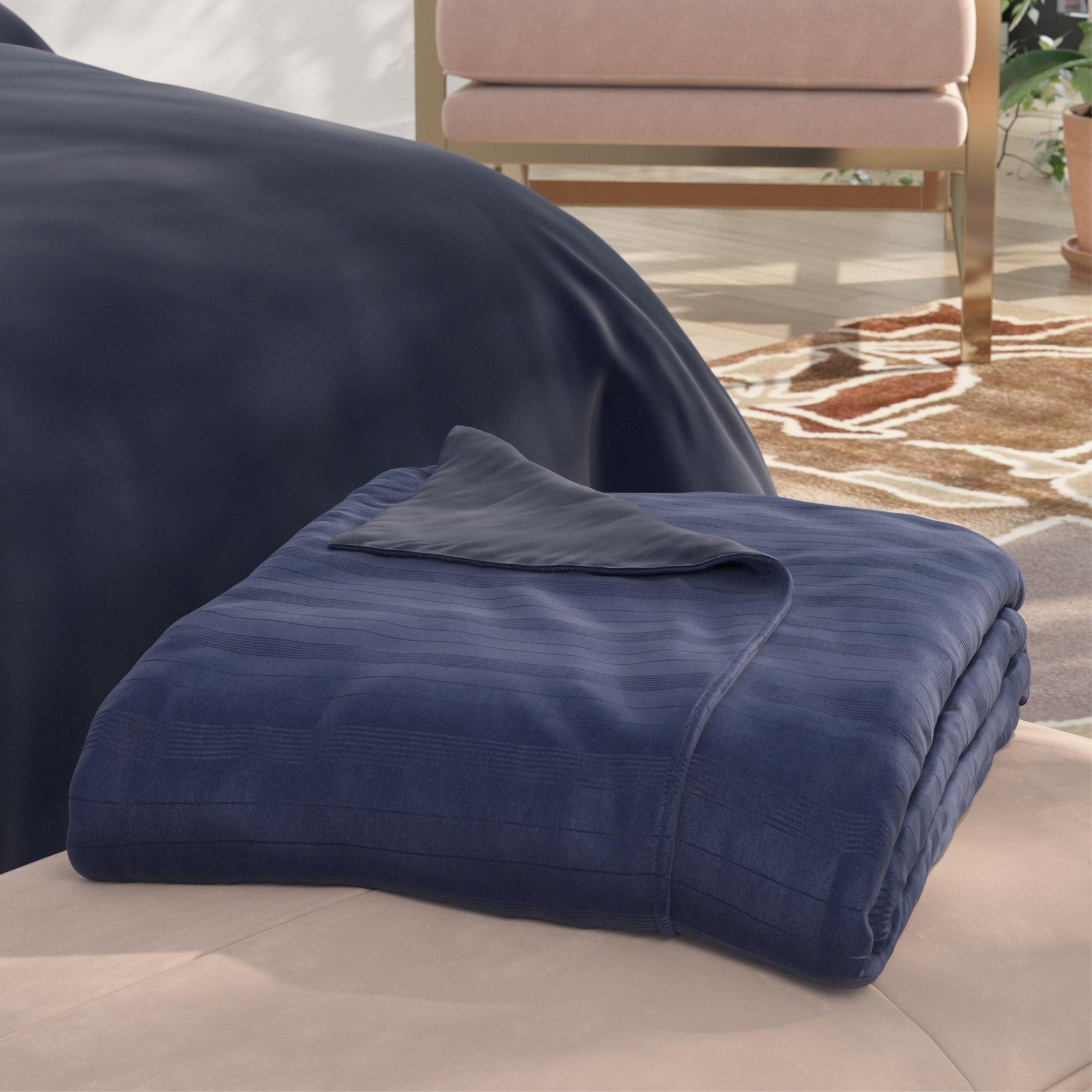Image of a neatly folded Midnight/Celestial Duvet Cover + Cooling with the Midnight side facing up and a corner of the Celestial side folded back on a tan stool at the foot of a bed
