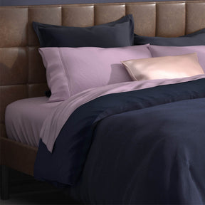 Image of a bed with lilac sheets and the Midnight/Celestial Duvet Cover + Cooling and Pillow Shams + Cooling with the Midnight side facing up
