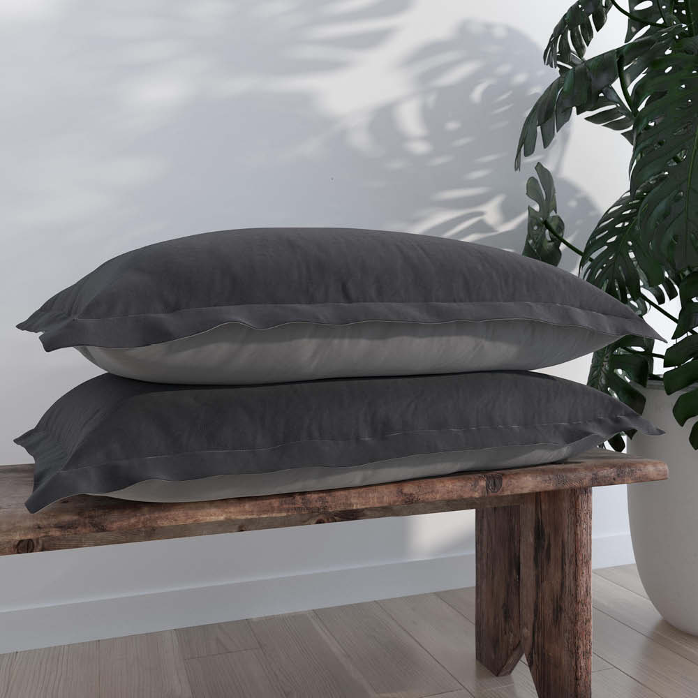 Image of two Shadow/Dove Gray Pillow Shams + Cooling on pillows stacked on a wooden bench