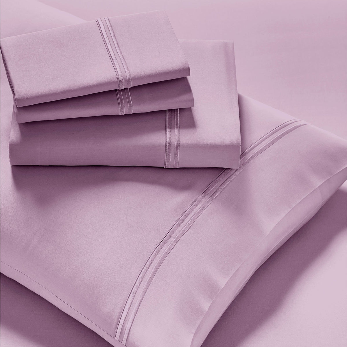 Image showcasing entire Lilac Refreshing TENCEL™ Lyocell Sheet Set. The image includes: a fitted sheet on the bed, a pillowcase on a pillow, a neatly folded flat sheet, and two neatly folded pillowcases.