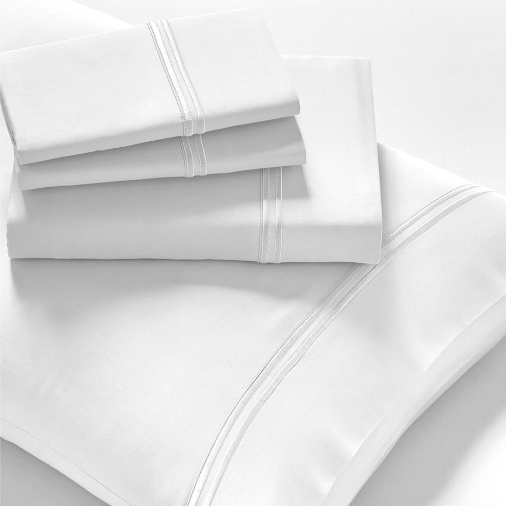 Image showcasing entire White Refreshing TENCEL™ Lyocell Sheet Set. The image includes: a fitted sheet on the bed, a pillowcase on a pillow, a neatly folded flat sheet, and two neatly folded pillowcases.