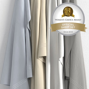 Image of all four color ways of Supima® Cotton Sheet Set hanging in order of Light Blue, Ivory, White, Dove Gray with a sticker in the top right corner saying "Women's Choice Award Official Sheet Set Since 2018"