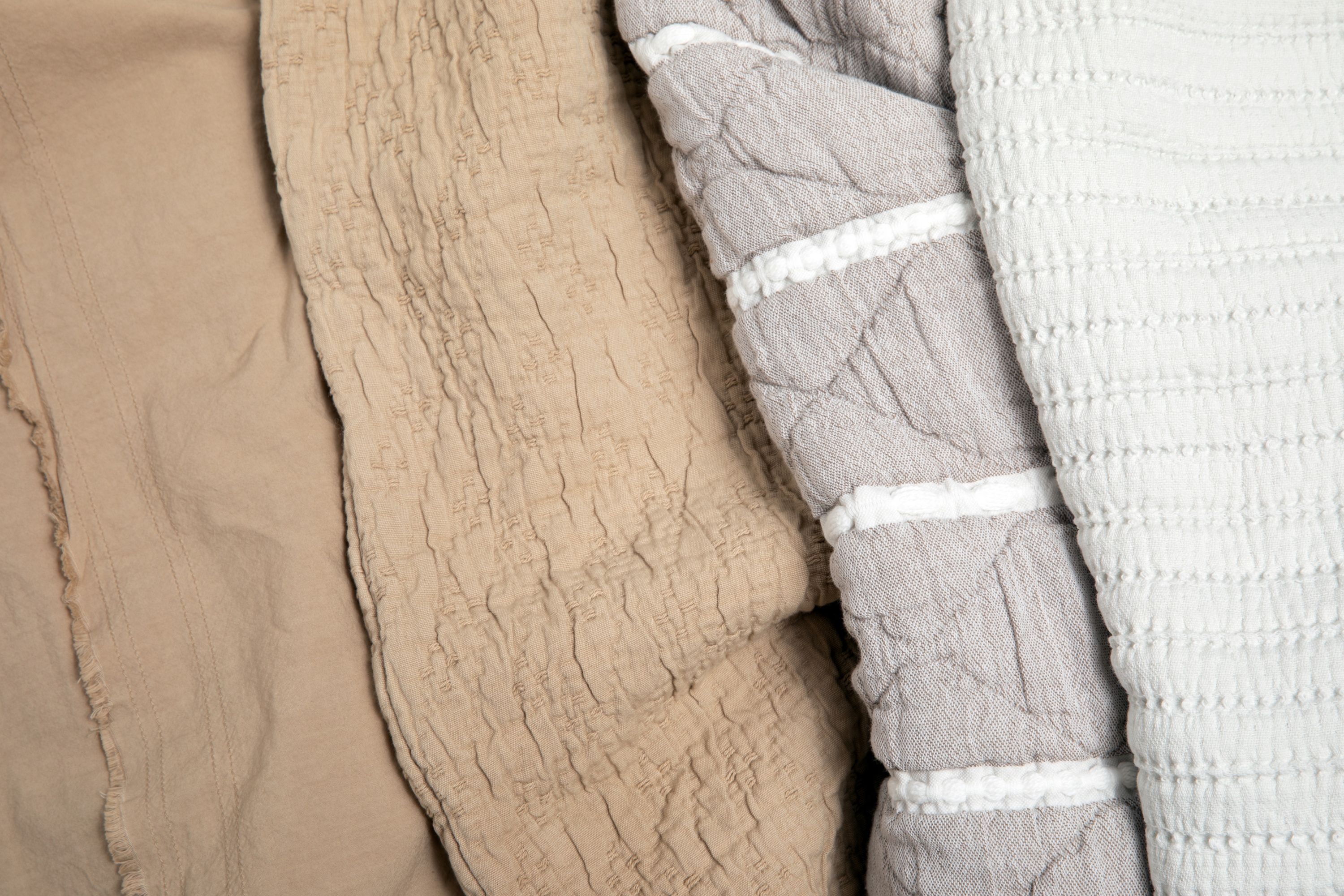 Image of four Dr. Weil products side-by-side. From left to right: Ochre Garment Washed Sheets, Ochre Wave Coverlet, Heritage Quilt, Ecru Ridgeback Coverlet