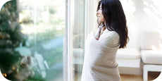Image of a woman wrapped in a Bright White Everyday Cotton Coverlet staring out a wintery window